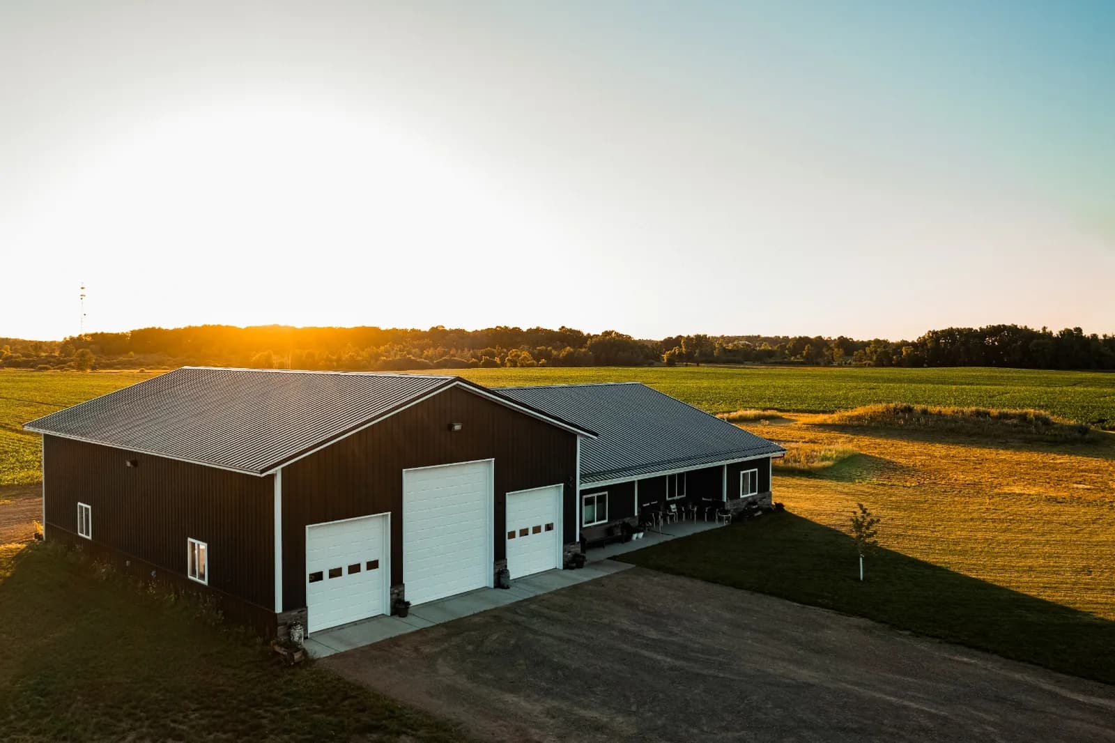 Sherman Buildings barndominium with three garage bays and covered porch at sunset