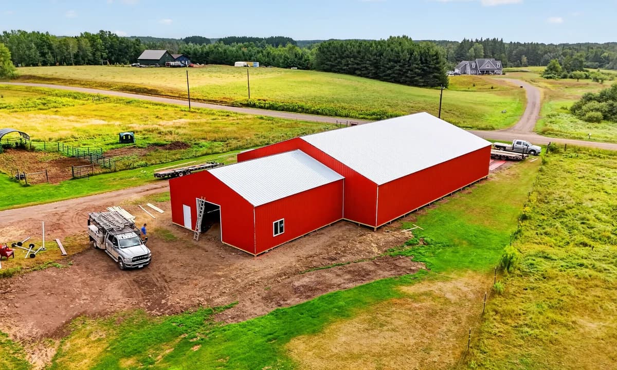 Aerial view of a red agricultural building with a white roof beside farm pastures