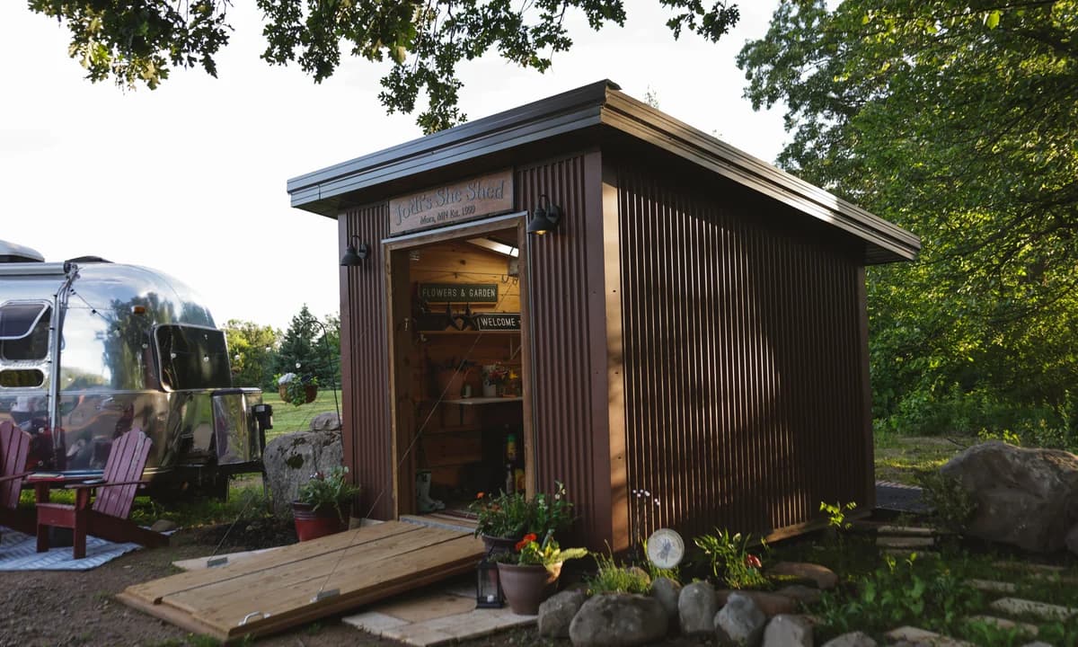 Small brown she shed with an open doorway and wooden access ramp in a garden setting