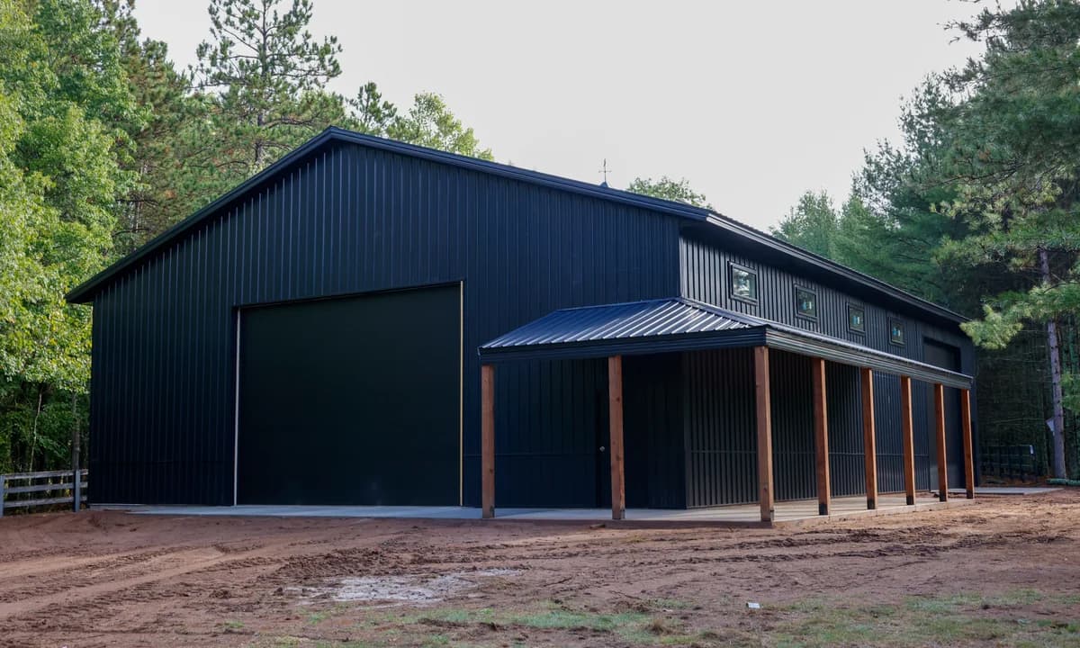 Dark post-frame storage building with a large overhead door and covered side porch