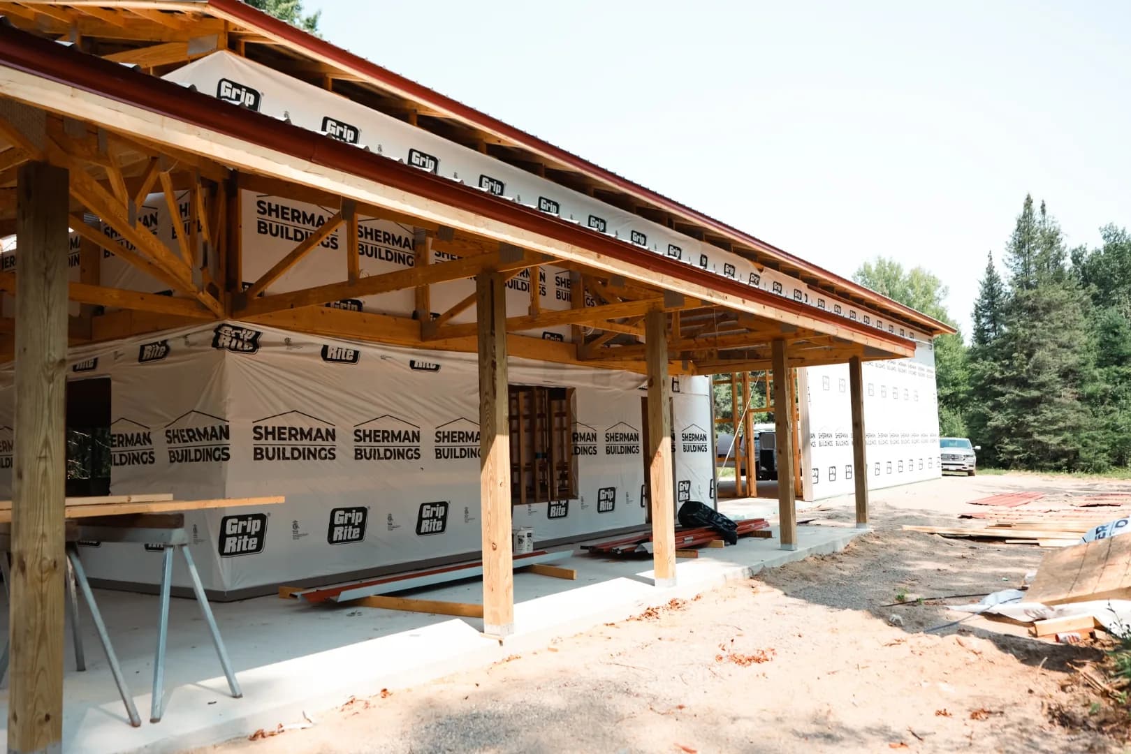 Sherman Buildings post frame build under construction with exposed timber posts, trusses, and house wrap