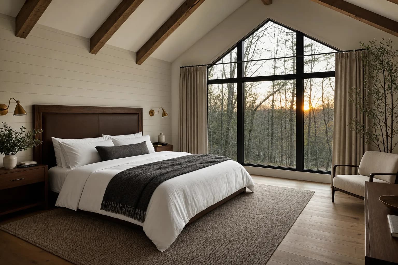 Primary suite bedroom with vaulted ceiling, exposed beams, large picture window and wood floors in a Sherman Buildings turnkey custom barndominium