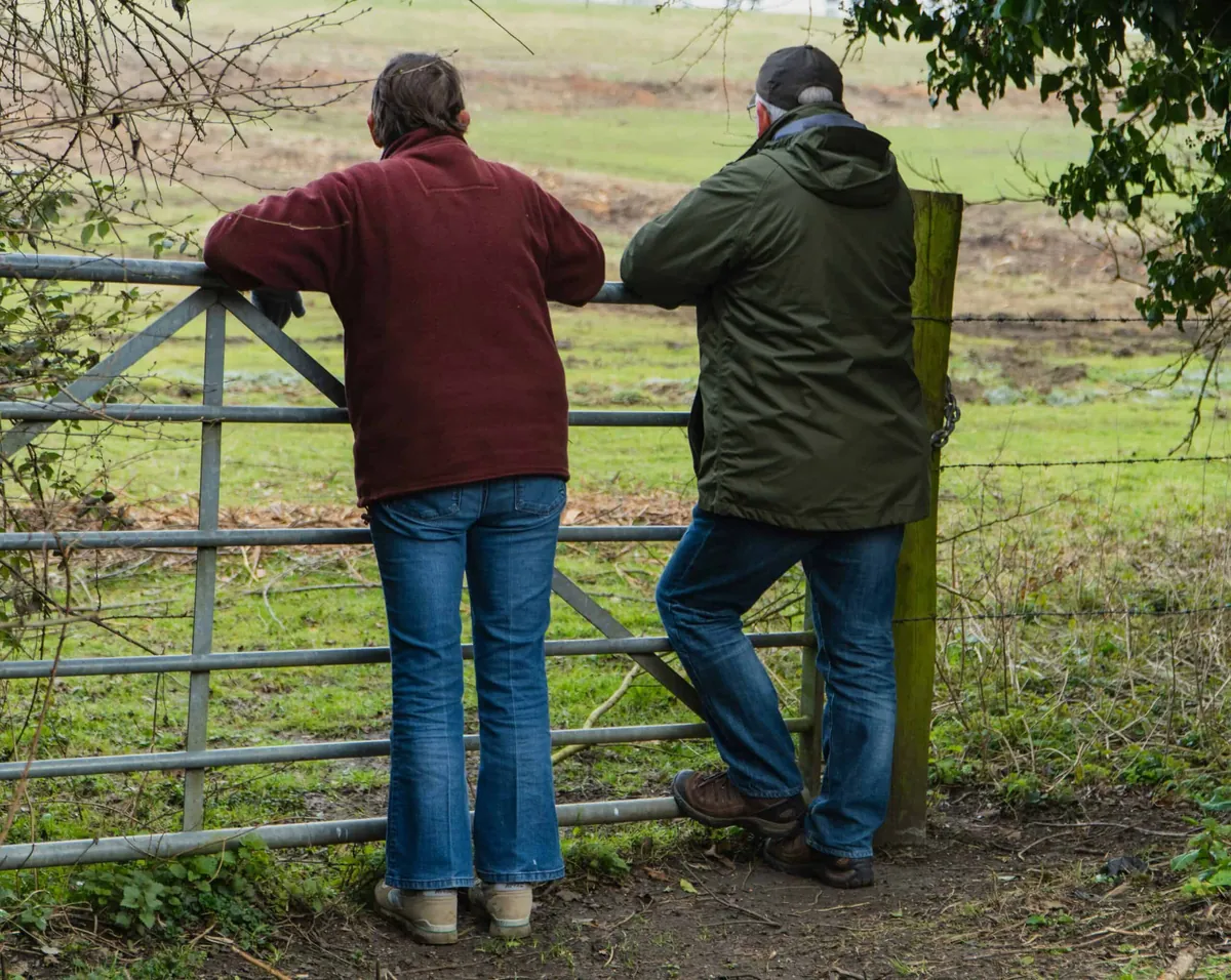 two people leaning on a fence in front of a field