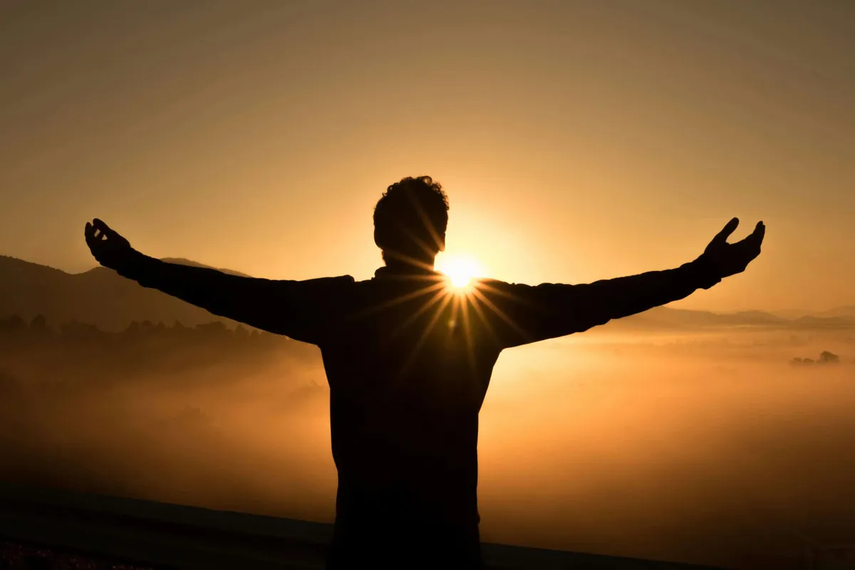 man with outstretched arms at sunrise 
